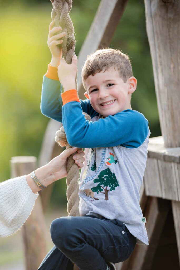 boy smiling at camera whilst swinging  on a rope in a play area during an outdoor family photography session in worcestershire