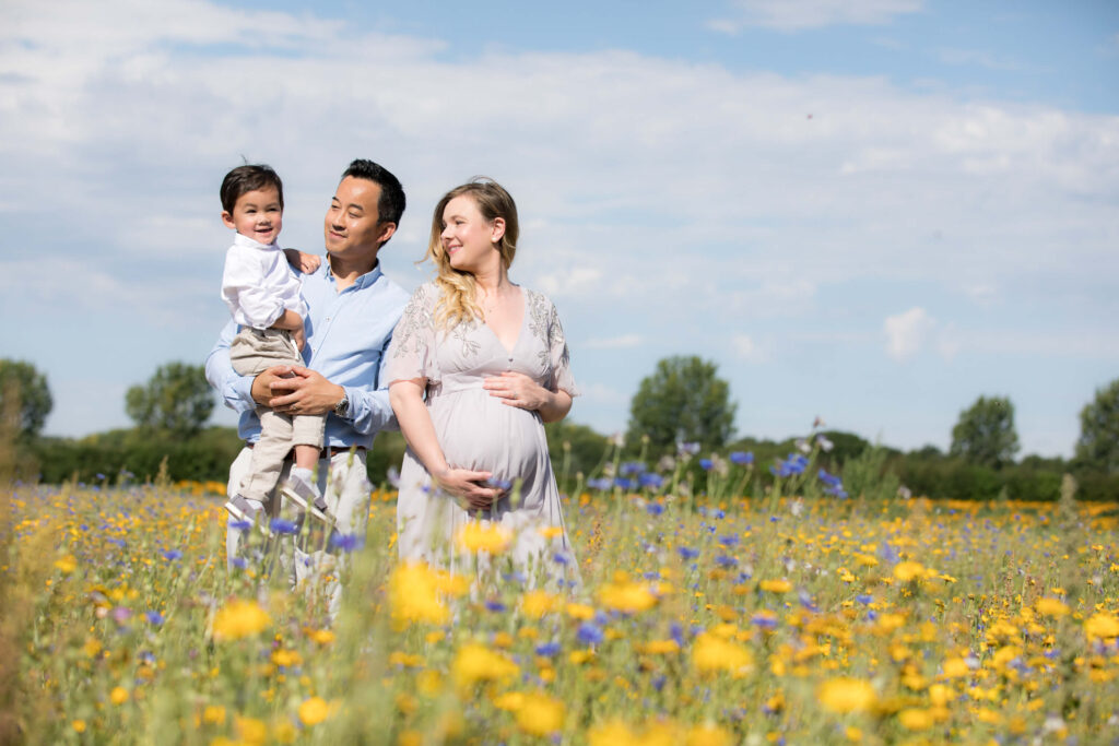 couple with toddler in arms in yellow flower field during maternity famly photography session
