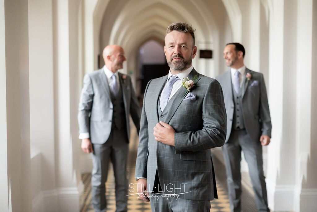 groom with two best men standing slightly behind him indoor in cloisters at stanbrook abbey