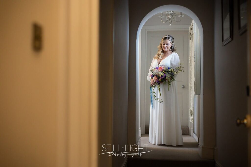 bride holding pink and green flowers standing in corridor in brides manor stanbrook abbey