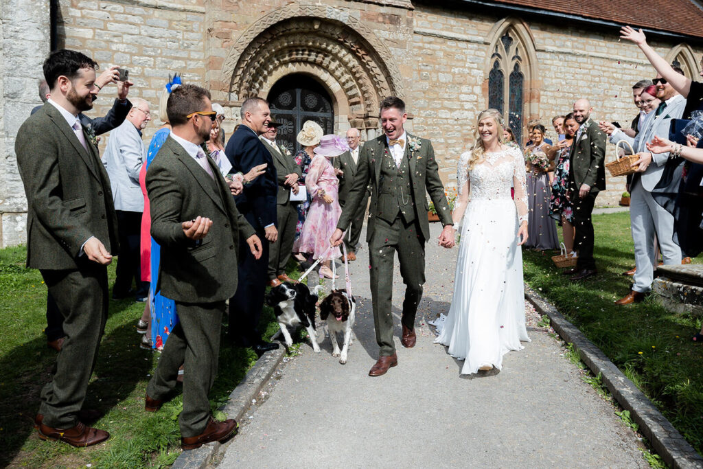 bride and groom exiting church with their two dogs, confetti being thrown by guests
