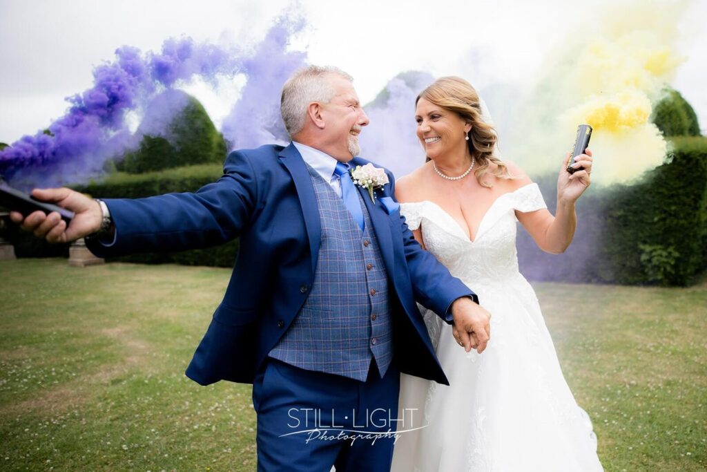 bride and groom laughing together holding purple and yellow smoke grenades