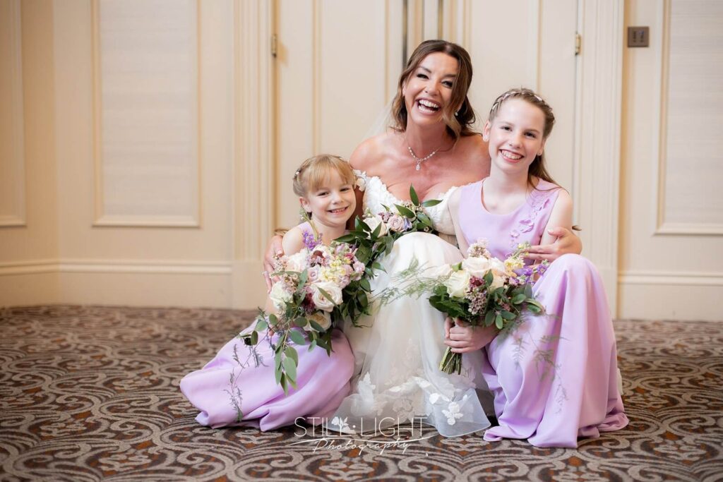 bride with two daughters in lilac dresses looking and smiling at camera