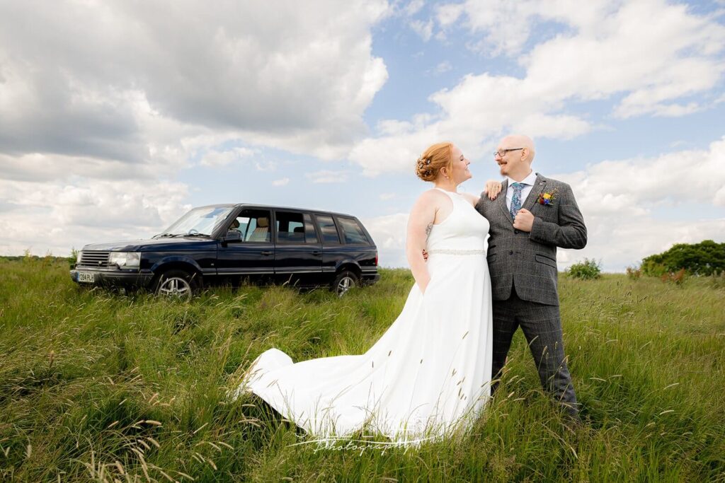 bride and groom standing together in front of jeep during estate tour at wootton park