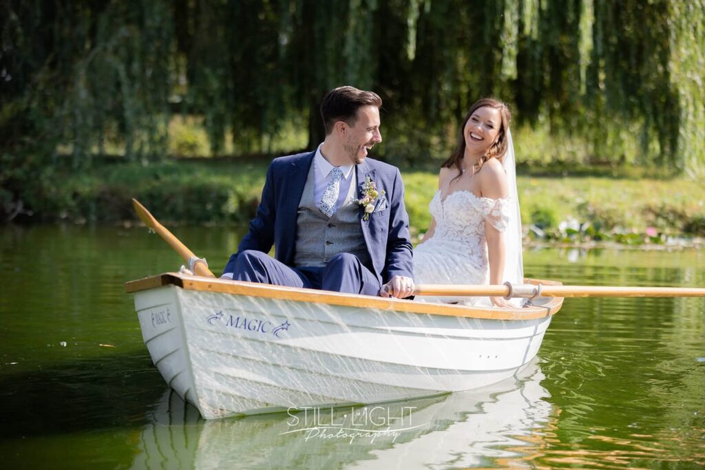 bride laughing at groom whilst sat in rowning boat on wedding day at wootton park