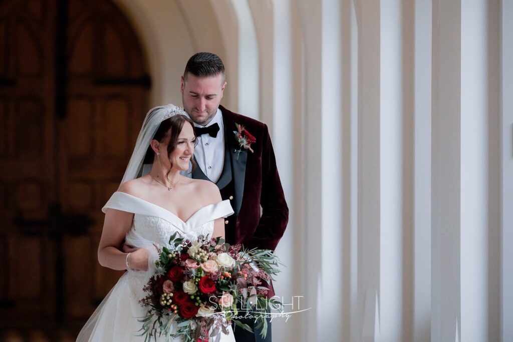 couple stand together for photo on their wedding day indoor in cloisters at stanbrook abbey