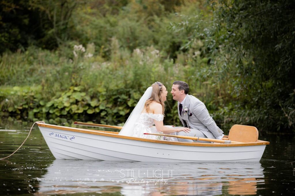 bride and groom laughing at each other whilst in rowing boat on wedding day at wootton park