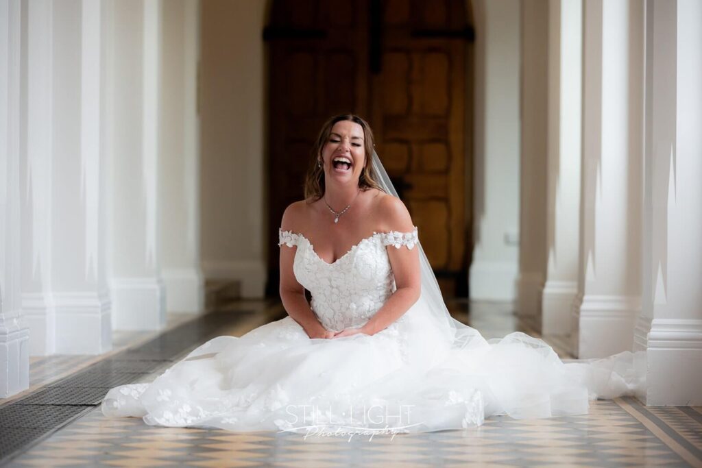 bride sitting on floor laughing indoor in cloisters at stanbrook abbey