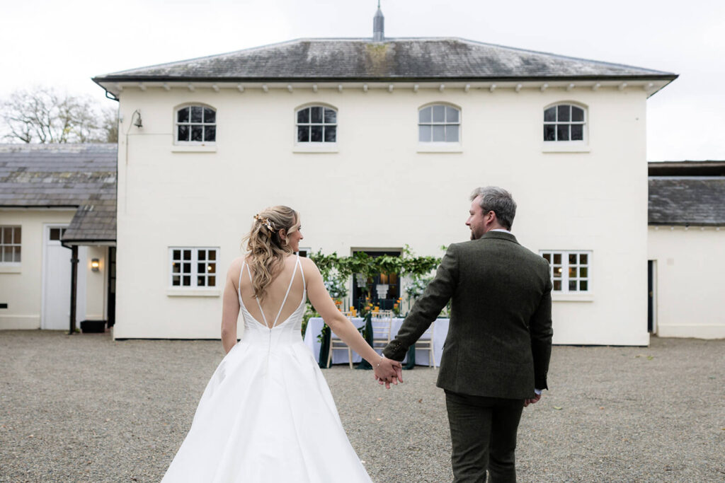 the coach house at hopton court with bride and groom wlking towards it away from camera