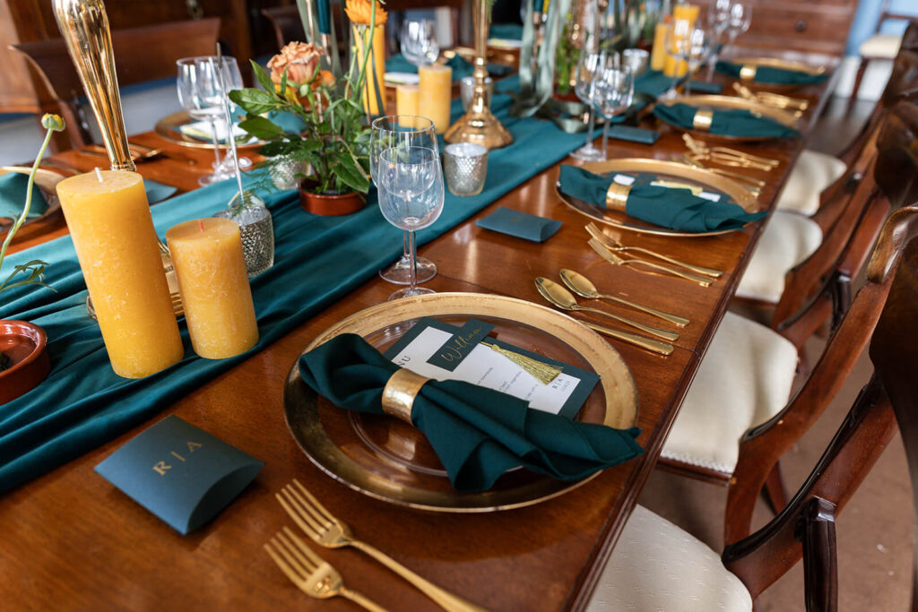 dinner table set up with teal table runner, dark green and yellow candles and orange and yellow flowers