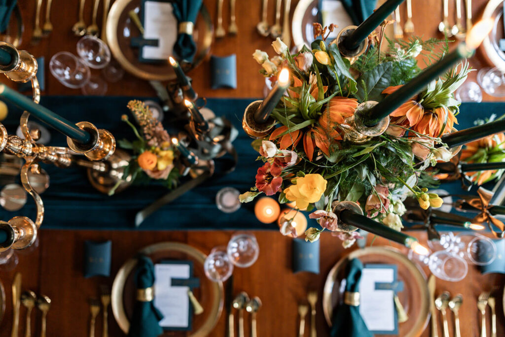 image taken from above of dinner table set up with teal table runner, dark green and yellow candles and orange and yellow flowers