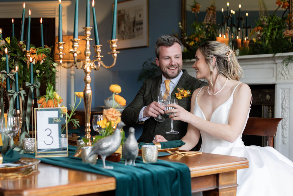 bride and groom toast with wine glasses whilst sitting at dinner table in hopton court main house