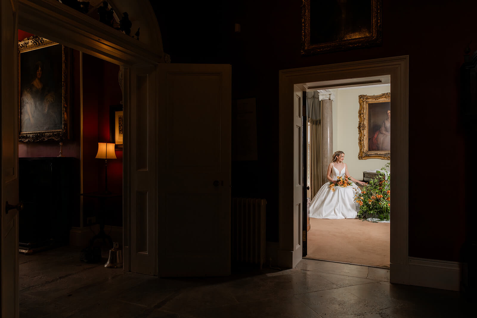 bride sits at piano with bouquet on her lap image taken through doorway in hopton court lobby