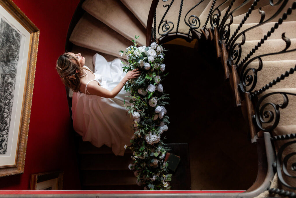 taken from above of bride walking up spiral staircase with iron bannister towards window