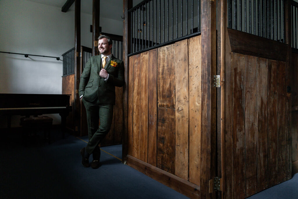 man wearing green tweed suit standing leaning against stable door in newley refurbished stables at hopton court