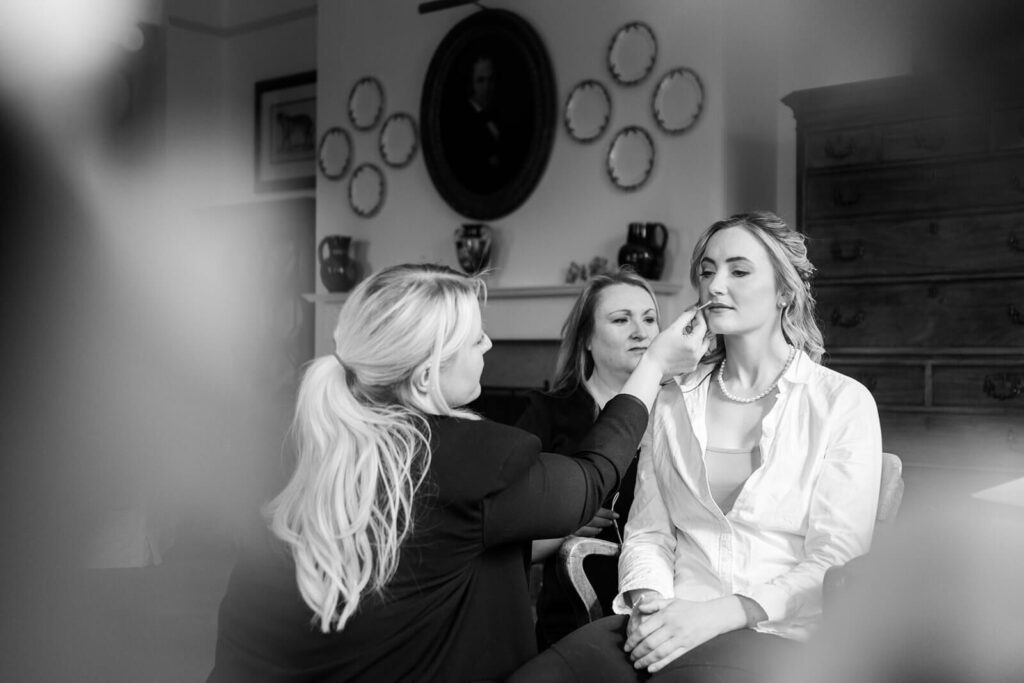 black and white image of bride having makeup and hair done in the lounge at hopton court
