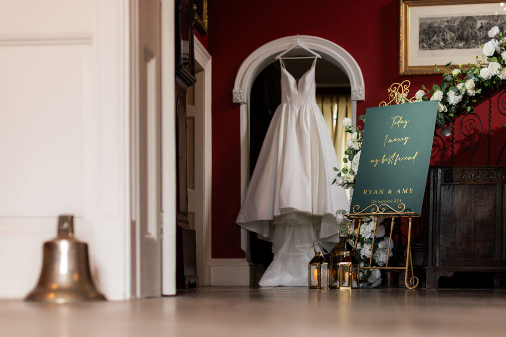 wedding dress hanging from archway in hopton court wedding venue with welcome sign on gold easel next to it
