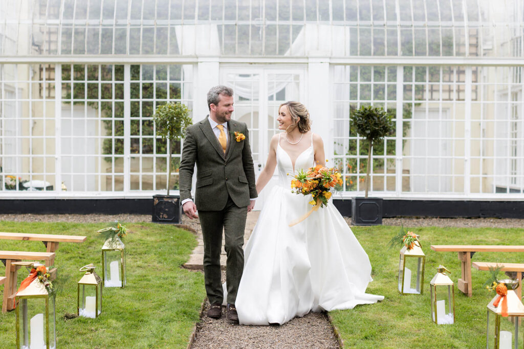bride and groom walking towards camera looking at each other inf ront of orangery at hopton court wedding
