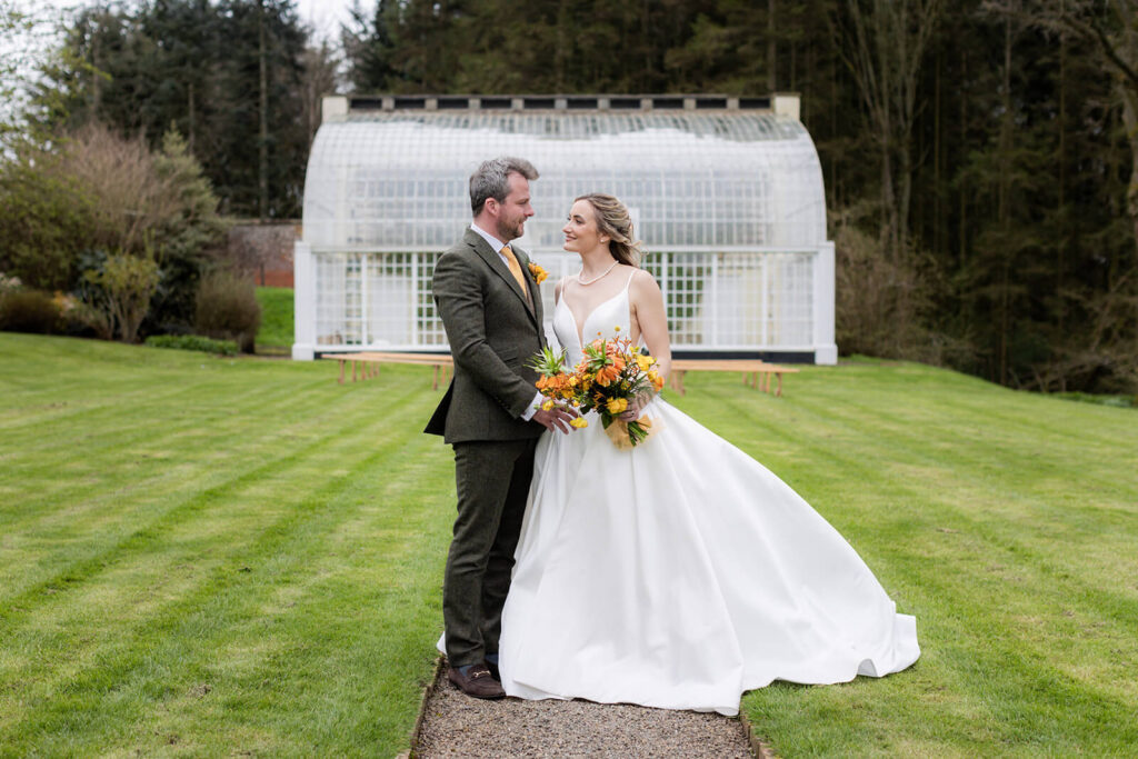 bride and groom standing together in front of orangery at hopton court wedding
