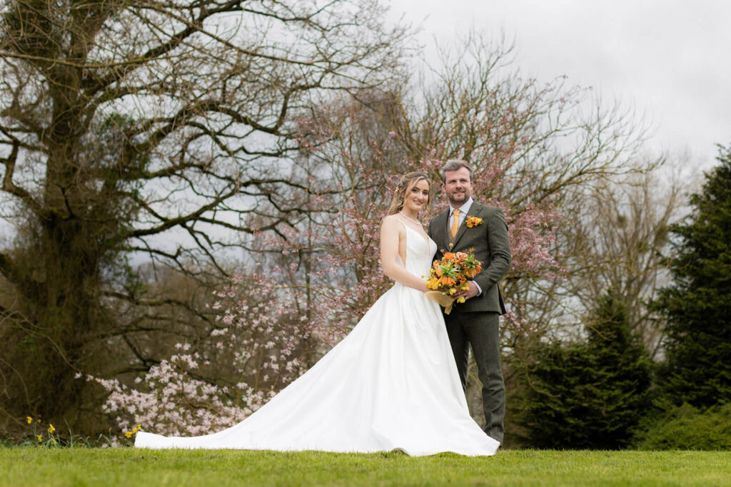 bride and groom standing together looking at camera with magnolia tree behind them