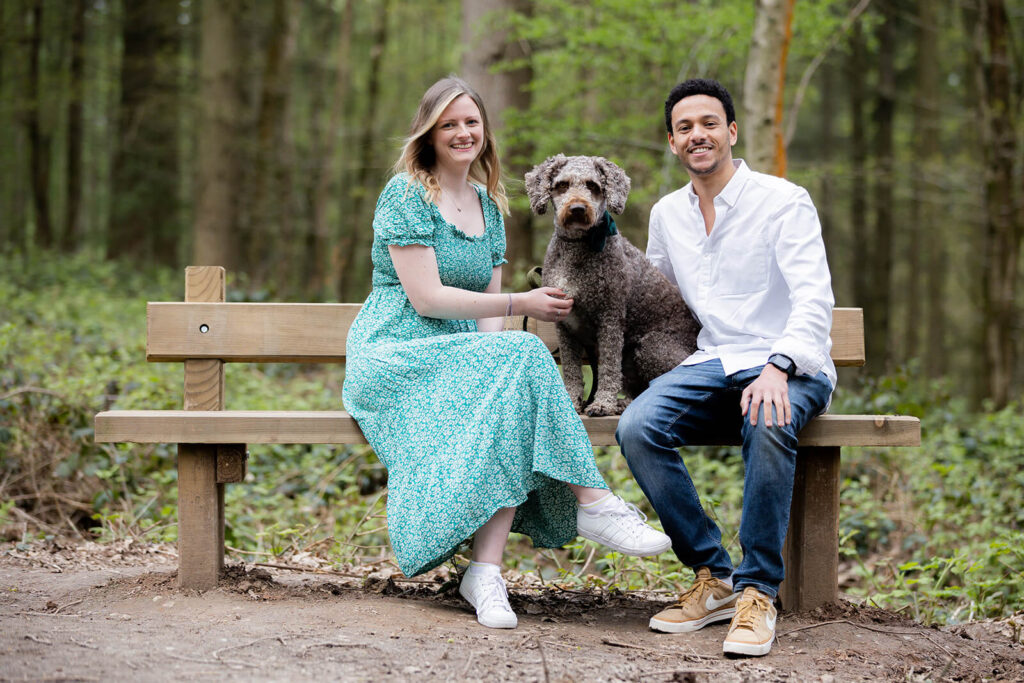 couple sitting on bench with their dog during engagement session in a woodland setting