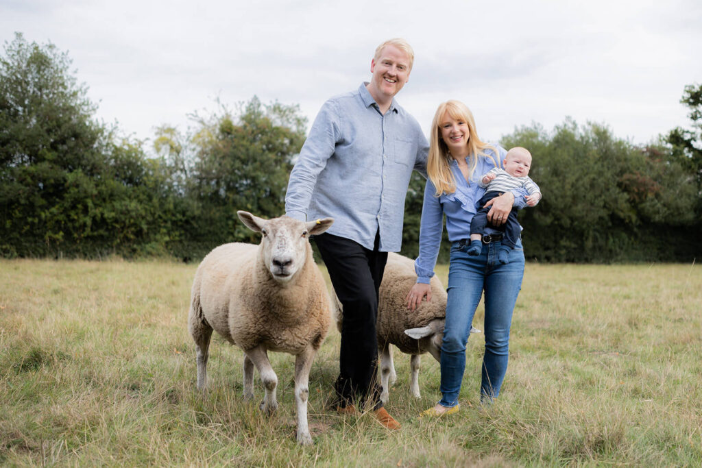 couple and baby with 2 sheep standing in field looking at camera