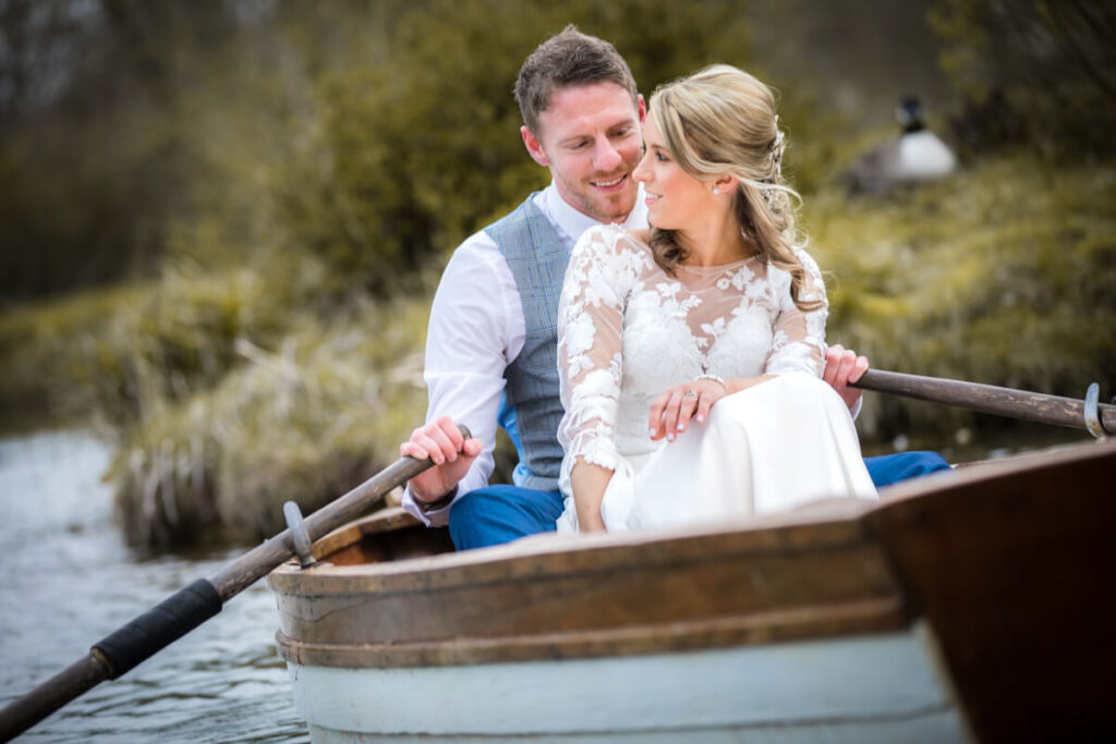 bride and groom cuddling sitting in rowing boat on wedding day at wootton park