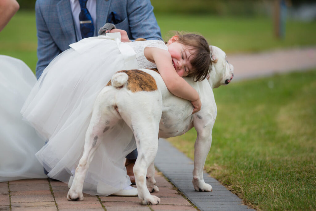 little girl in white flowergirl dress hugging her dog