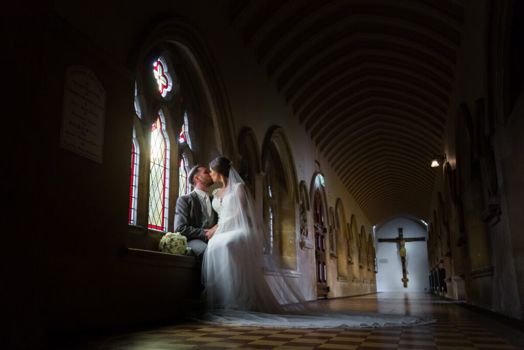 bride and groom kissing sat on windowsill in corridor at stanbrook abbey