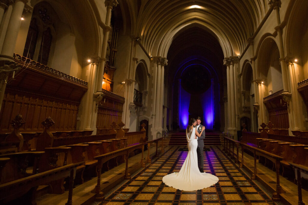 bride and groom posing with bride's back to camera in aisle at Callow Great Hall at Stanbrook Abbey