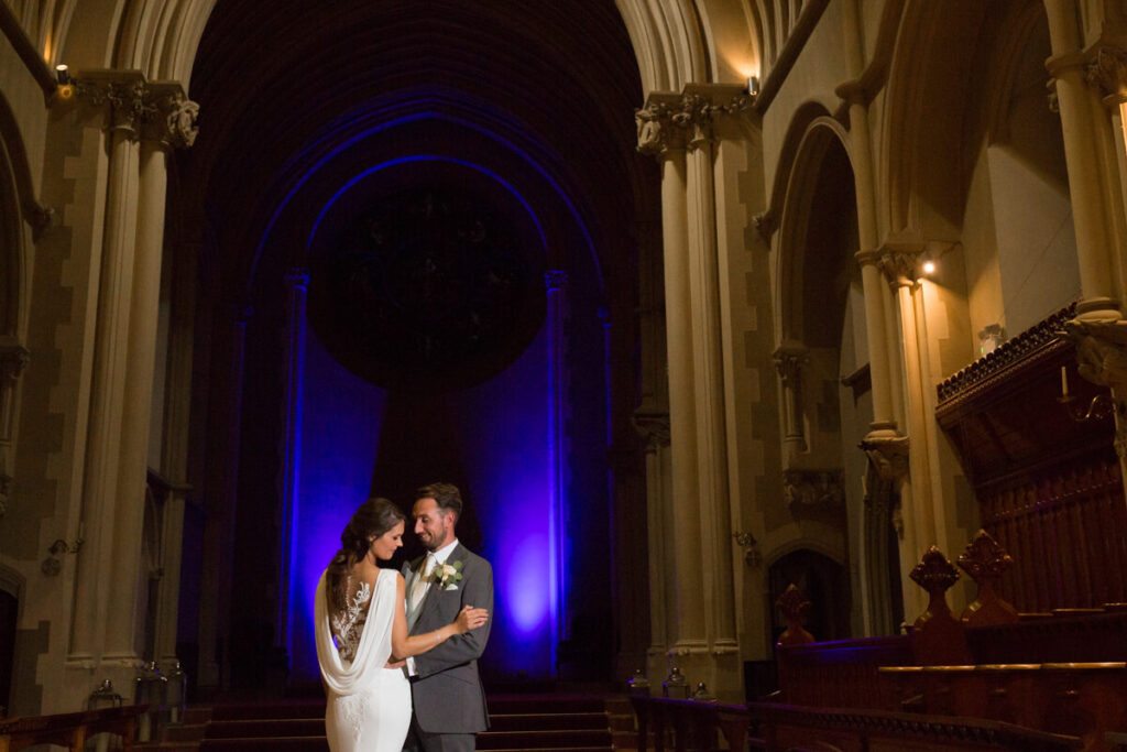 bride and groom cropped at hips standing against dark blue background of Callow Great Hall at Stanbrook Abbey