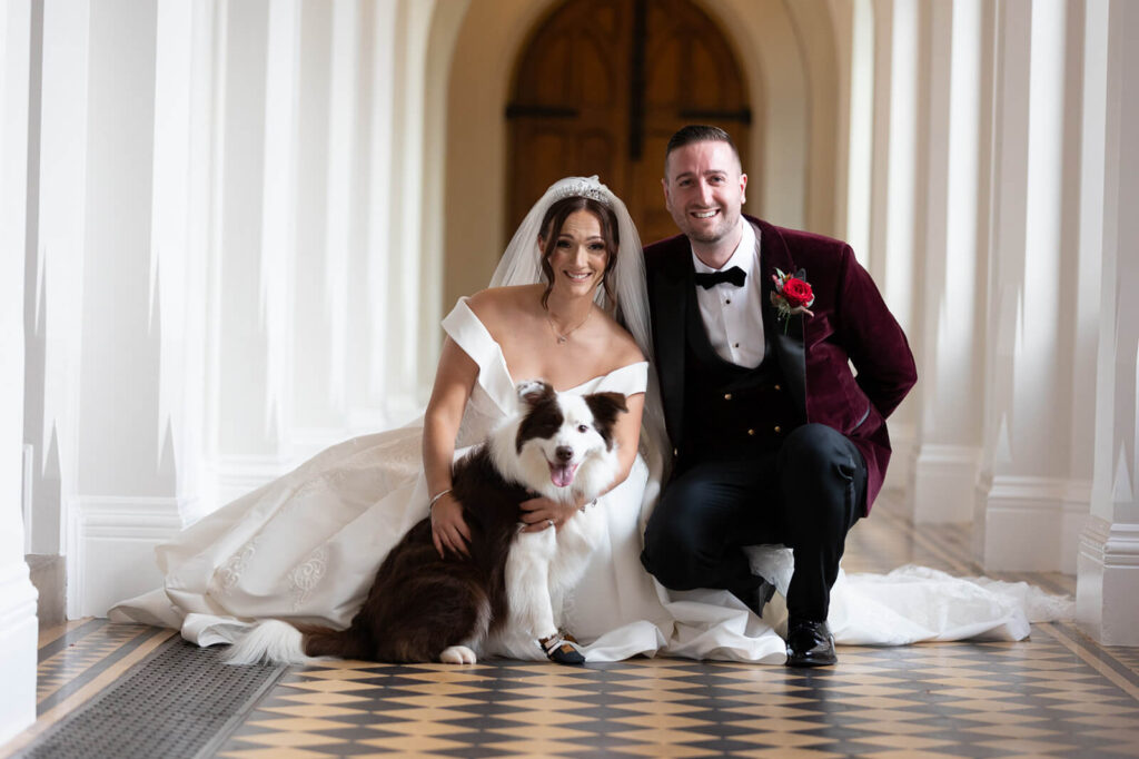 bride and groom crocuhing with their dog all looking at camera taken at stanbrook abey hotel, a dog friendly wedding venue