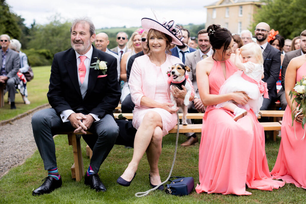 wedding guests sitting on benches with a little jack russell terrier during dog friendly wedding day at Hoption Court